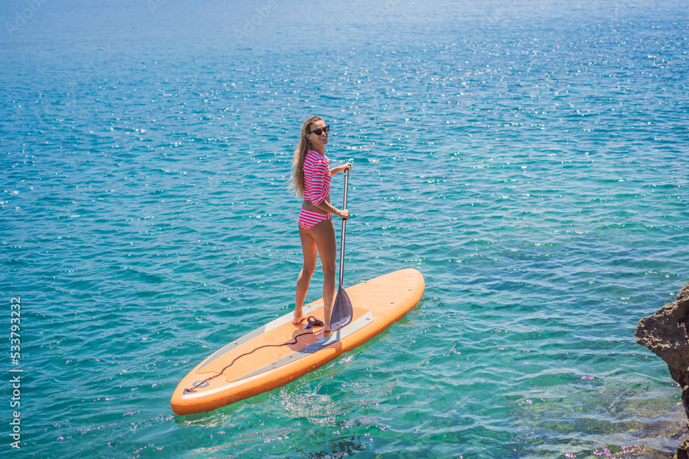 Young women Having Fun Stand Up Paddling in blue water sea in Montenegro. SUP. girl Training on Paddle Board near the rocks Young women Having Fun Stand Up Paddling in blue water sea in Montenegro. SUP. girl Training on Paddle Board near the rocks