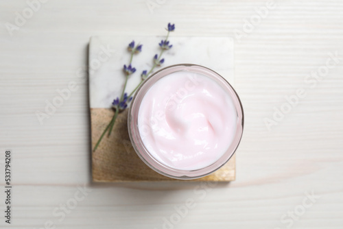 Jar of hand cream and lavender flowers on white wooden table, top view