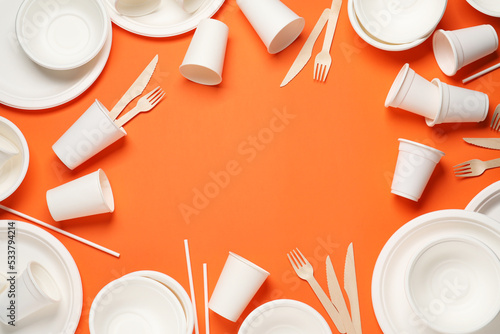 Frame of disposable tableware on orange background, flat lay. Space for text photo