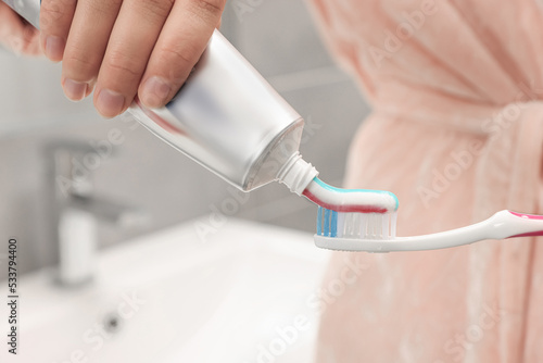 Woman applying toothpaste on brush in bathroom  closeup