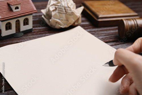 Woman signing last will and testament at wooden table, closeup