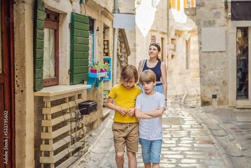Mom and son travelers enjoying Colorful street in Old town of Kotor on a sunny day, Montenegro. Travel to Montenegro concept Portrait of a disgruntled girl sitting at a cafe table © galitskaya