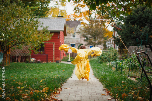 A child in long golden dress and wings leaps through garden photo