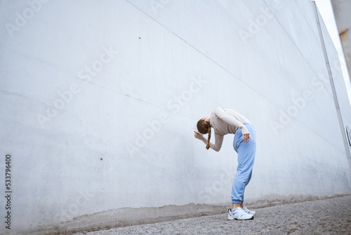 Girl in a blue pants stretching and dancing against grey wall photo