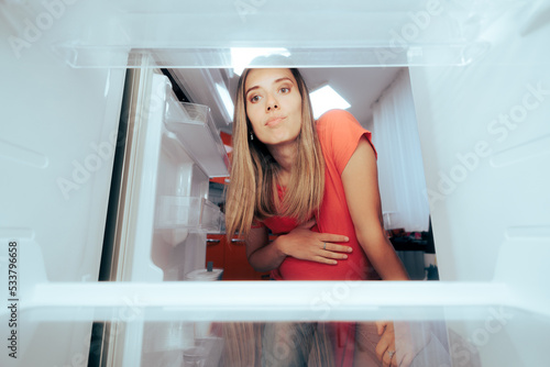 Pregnant Woman Craving for Food Looking at an Empty Fridge. Mother to be having nothing to eat considering ordering a meal in 