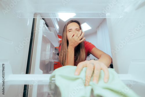 Unhappy Woman Cleaning Stinky Dirty Fridge with a Cloth. Housewife trying to get the rotten spoiled odor out of the freezer
 photo