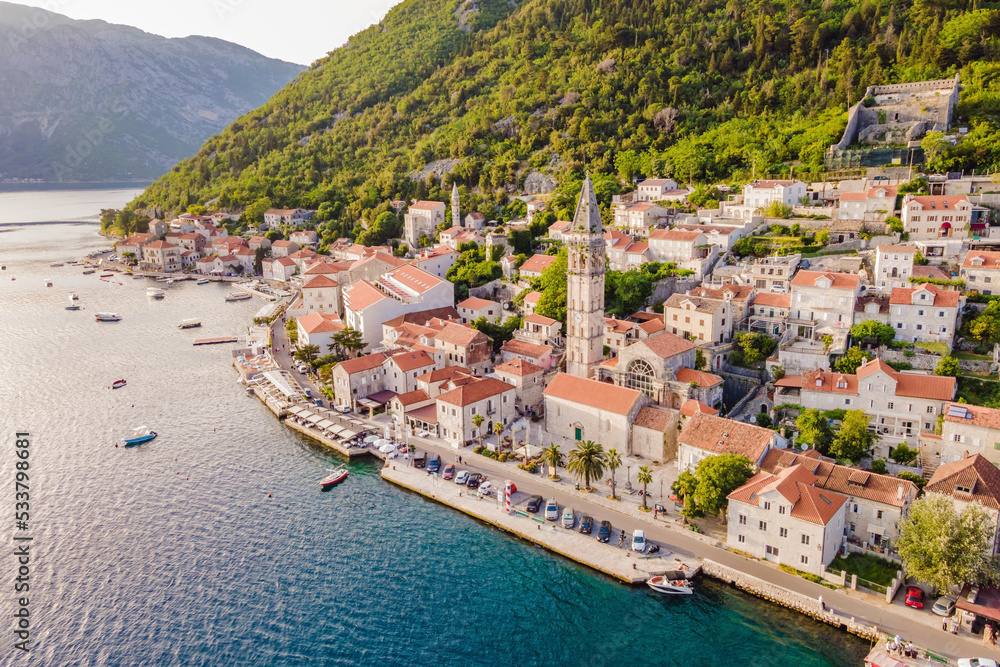 Scenic panorama view of the historic town of Perast at famous Bay of Kotor with blooming flowers on a beautiful sunny day with blue sky and clouds in summer, Montenegro, southern Europe Portrait of a