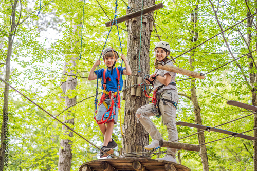 Mother and son climbing in extreme road trolley zipline in forest on carabiner safety link on tree to tree top rope adventure park. Family weekend children kids activities concept Portrait of a