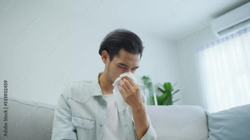 Asian handsome male having running nose and sneezing in living room. Asian handsome male having running nose and sneezing in living room.