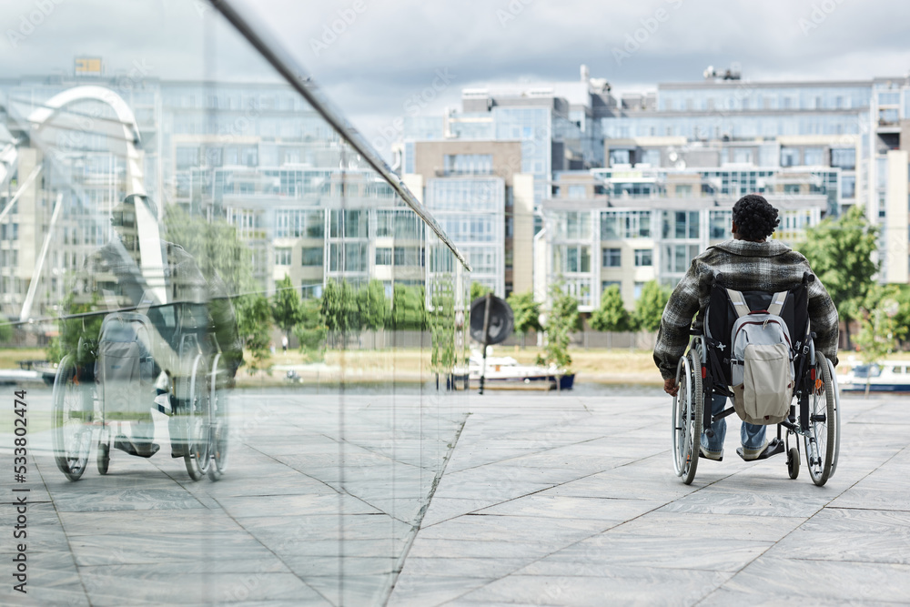 Back view of black woman in wheelchair outdoors with city skyline in background, copy space