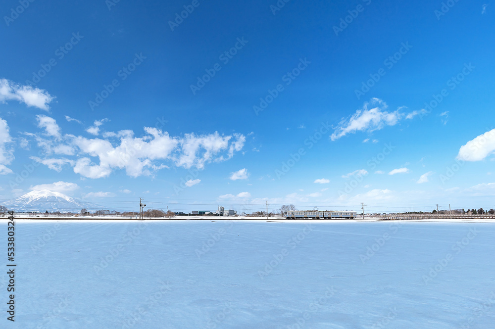 【青森県津軽】津軽平野の雪景色と岩木山、雪原を走るローカル鉄道