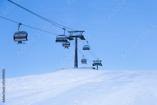 Ski chair lift on top of mountain, ski slope prepared for skiing, minimal style blue monochrome winter in Sheregesh ski resort. White snow, clear sky, cable road and small people on peak