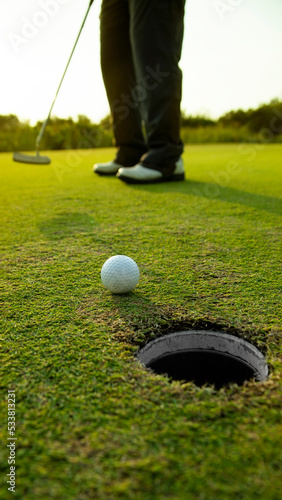 golfer putting a golf ball into a last hole on the green, golf course on summer sunset evening time