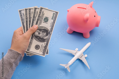 hand holding dollar banknote with piggy bank and airplane model, save money budget for travel or discount booking air ticket concept