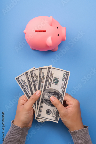 hand holding dollar money banknote with piggy bank save coin from top view or flat lay, blue desk background, saving money and invesment concept