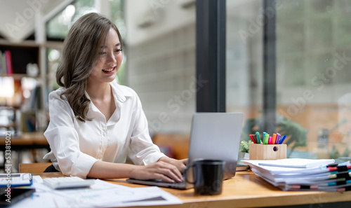Smiling young asian businesswoman working on a laptop at her desk in a bright modern lofe office
