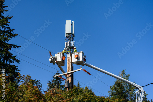 Two linemen working on a wireless communications radio and antenna installation using a bucket truck 