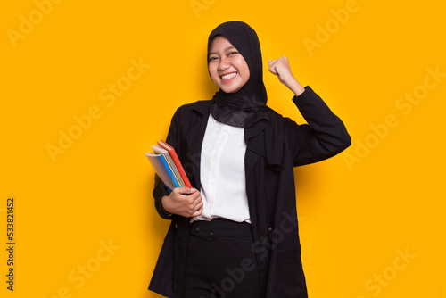 beautiful asian muslim business woman hug a book isolated on yellow background
