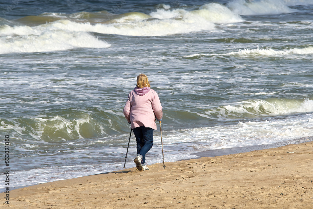 An elderly woman is engaged in Nordic walking. Health walking by the sea. Selective focus.