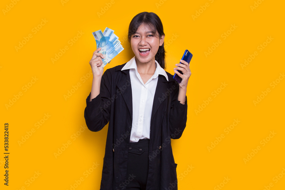 Asian business woman showing money and holding mobile phone isolated on yellow background
Asian business woman showing money and holding mobile phone isolated on yellow background