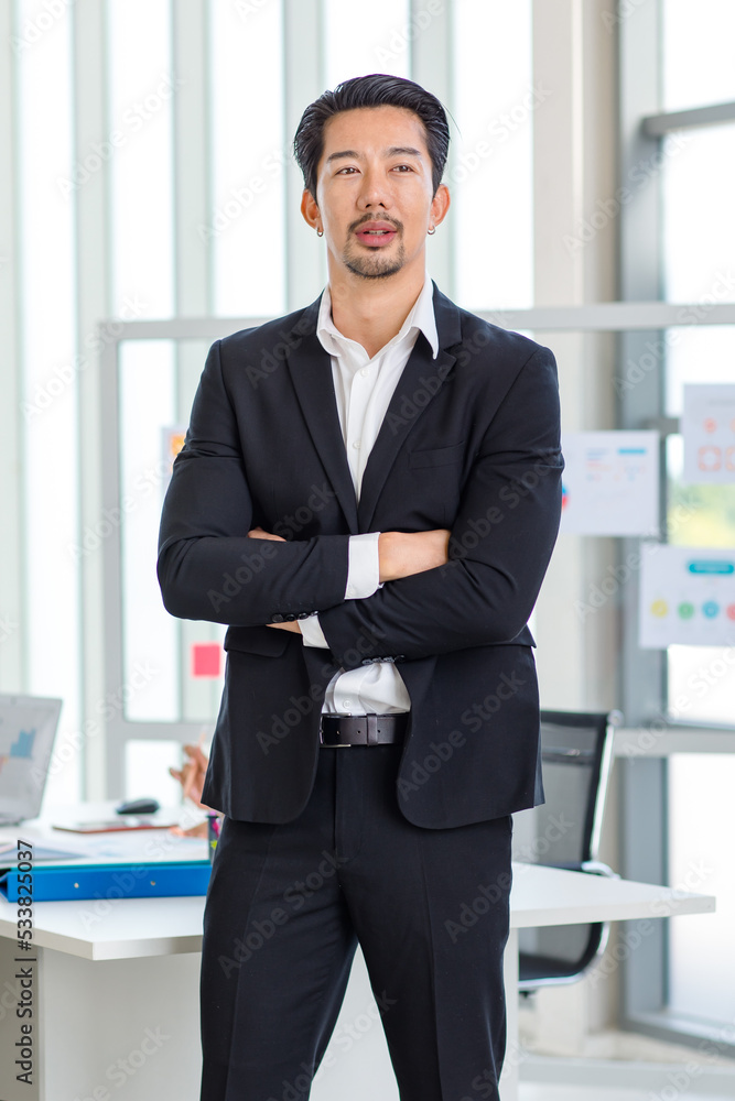 Millennial Asian professional successful young handsome bearded male businessman in formal suit standing posing crossed arms in company office workstation meeting room with information glass board Millennial Asian professional successful young handsome bearded male businessman in formal suit standing posing crossed arms in company office workstation meeting room with information glass board