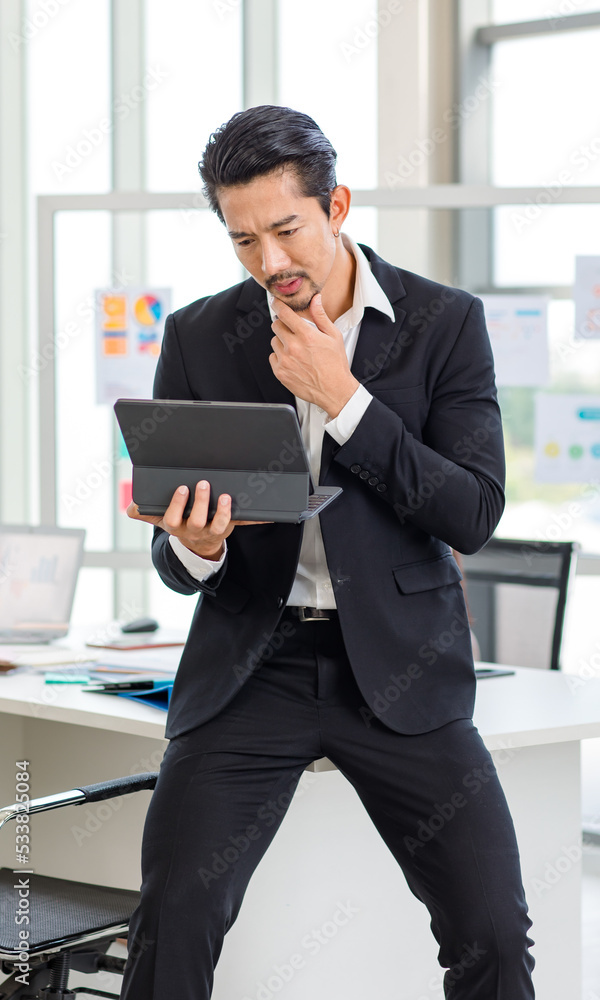 Millennial Asian professional successful bearded male businessman in formal suit sit on table browsing surfing internet via tablet computer in company office meeting room while colleagues discussing Millennial Asian professional successful bearded male businessman in formal suit sit on table browsing surfing internet via tablet computer in company office meeting room while colleagues discussing