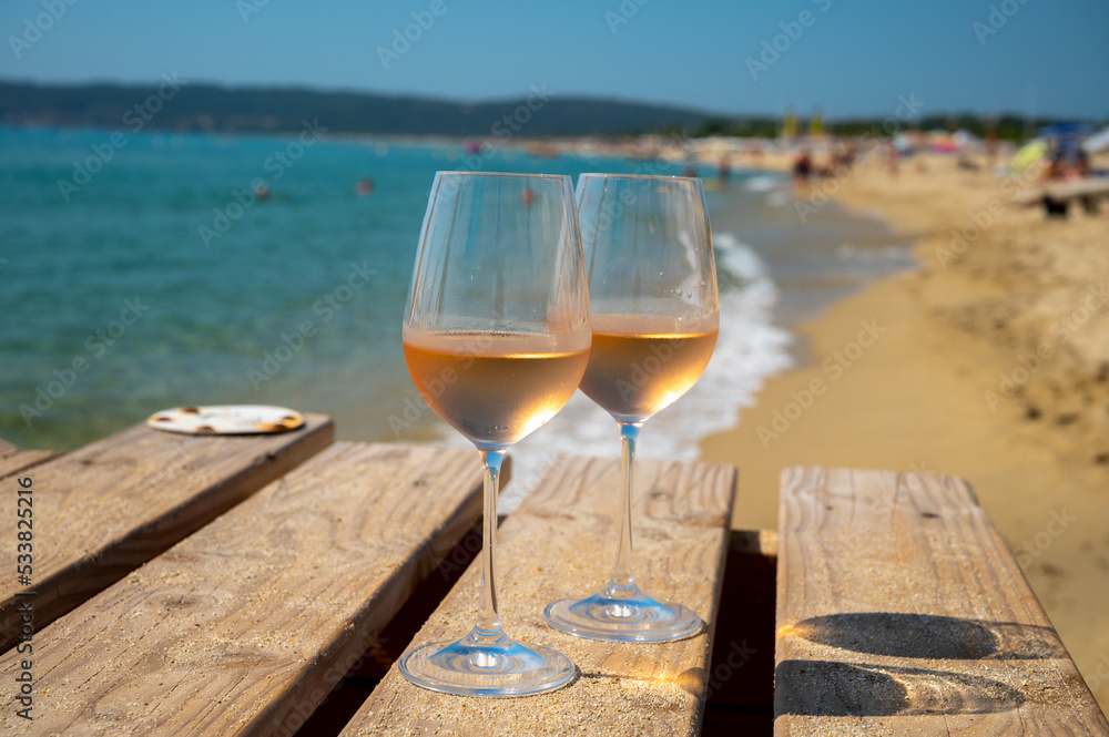 Glasses of cold rose wine from Provence served outdoor on wooden yacht pier with view on blue water and white sandy beach Plage de Pampelonne near Saint-Tropez, France Glasses of cold rose wine from Provence served outdoor on wooden yacht pier with view on blue water and white sandy beach Plage de Pampelonne near Saint-Tropez, France