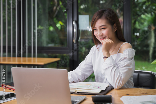 Young beautiful joyful woman smiling while working with laptop in office. Start-up office background.