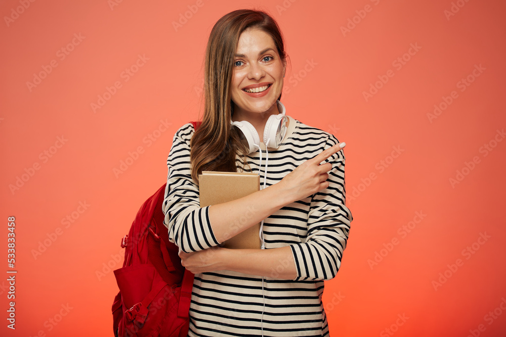 Smiling student with book and red backpack pointing finger away. isolated female portrait on pink background. Smiling student with book and red backpack pointing finger away. isolated female portrait on pink background.
