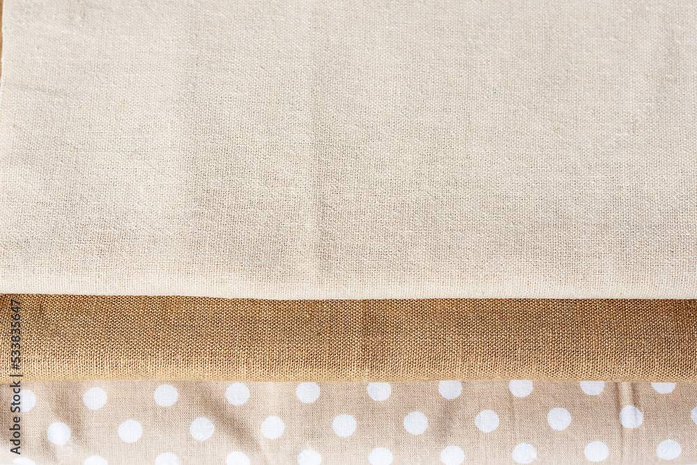 Fototapeta premium Natural linen raw organic cotton fabric. natural fabrics of ivory color - linen and cotton are stacked in a pile lie on a white background close-up
