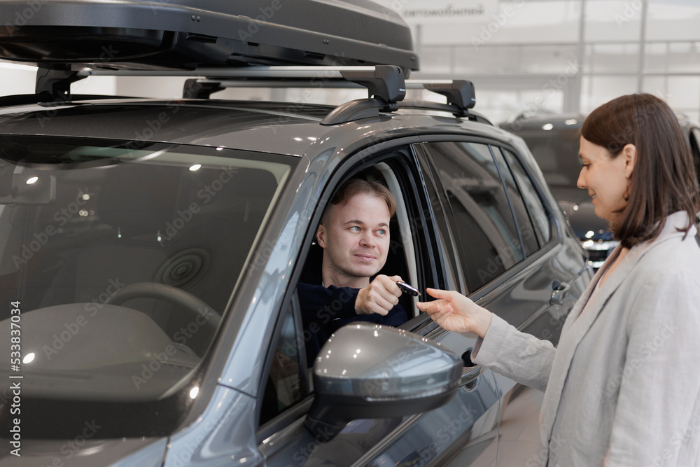 Fototapeta premium man buys a car at a car dealership. A female salesperson and car rental helps with the purchase. signing a trade-in contract and handing over keys, shaking hands. A successful man chooses a new car