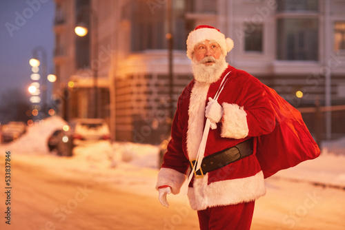 Portrait of Santa Claus walking in city at night and looking around, copy space