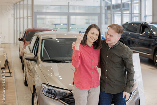 man and a woman couple in a car dealership buy or trade in. car rental or repair service. happy and successful married couple choose a new car on credit. happy two people holding keys and laughing