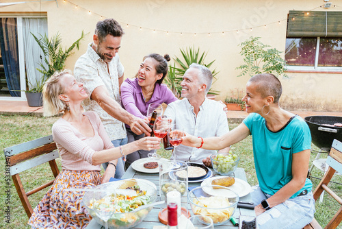 Canvas Print Group of happy middle-aged men and women toasting wine glasses at dinner event at house backyard