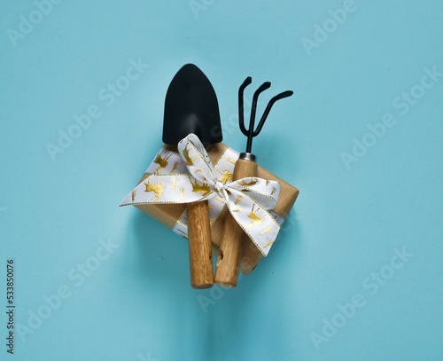 Christmas and new year composition. Garden tools, shovel and rake and gift box on a blue background. Top view with copy space. Banner