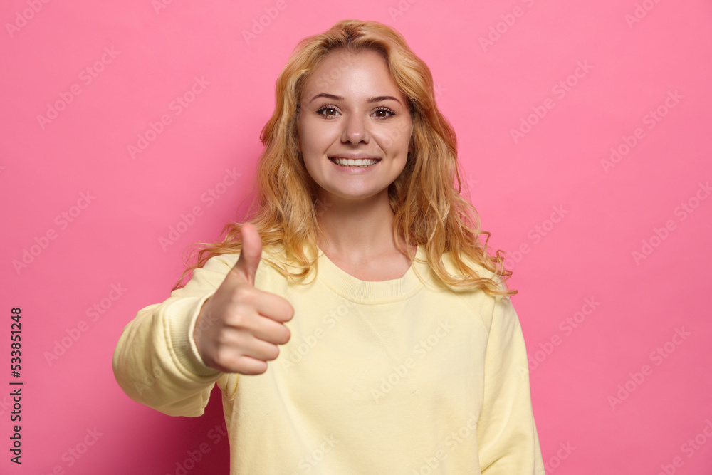 Happy young woman showing thumb up gesture on pink background Happy young woman showing thumb up gesture on pink background