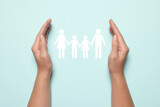 Woman holding hands around paper silhouette of family on light blue background, top view. Insurance concept