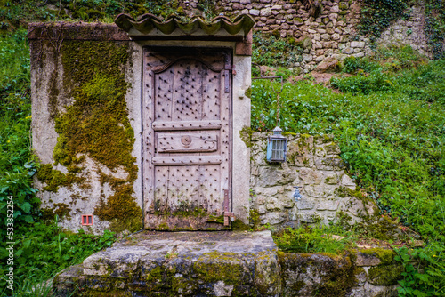 Fototapeta Naklejka Na Ścianę i Meble -  Medieval door and blue lantern with stone wall covered by green bushes in Thorrence, Ardèche (France)
