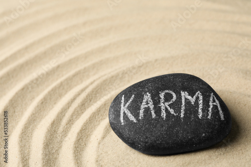 Stone with word Karma on sand, space for text