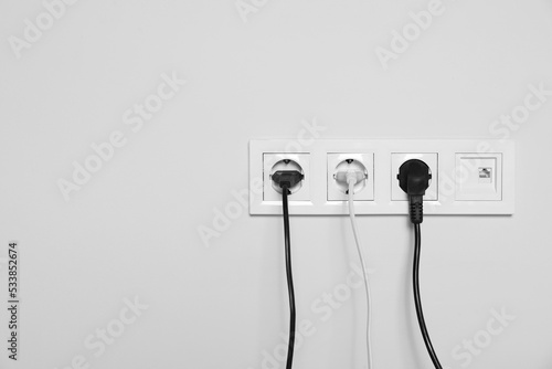 Power sockets with inserted plugs on white wall, space for text. Electrical supply