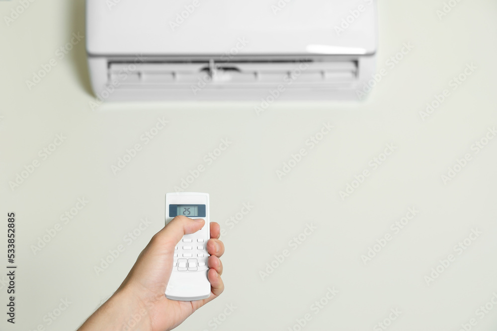 Fototapeta premium Man operating air conditioner with remote control indoors, closeup