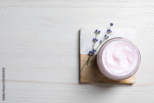 Jar of hand cream and lavender flowers on white wooden table, top view. Space for text