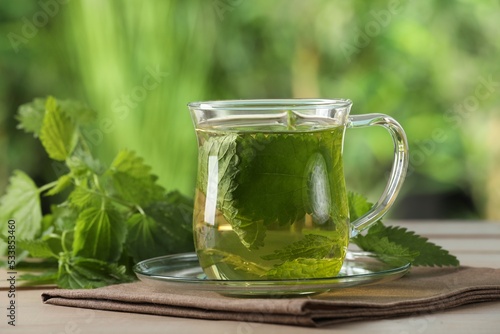 Glass cup of aromatic nettle tea and green leaves on wooden table outdoors