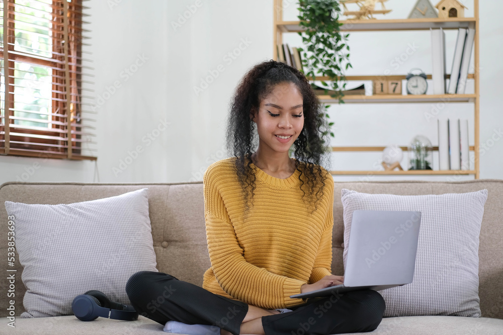 Beautiful Asian woman using laptop while headphones sitting on sofa at home Beautiful Asian woman using laptop while headphones sitting on sofa at home