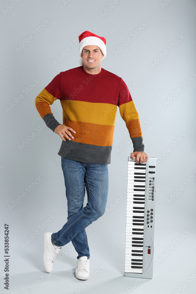 Man in Santa hat with synthesizer on light grey background. Christmas music Man in Santa hat with synthesizer on light grey background. Christmas music