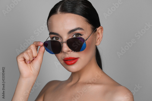 Attractive woman wearing fashionable sunglasses against grey background