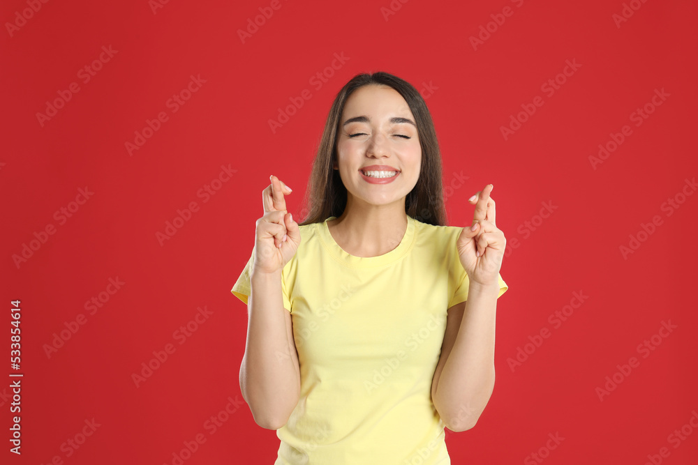 Excited young woman holding fingers crossed on red background. Superstition for good luck Excited young woman holding fingers crossed on red background. Superstition for good luck