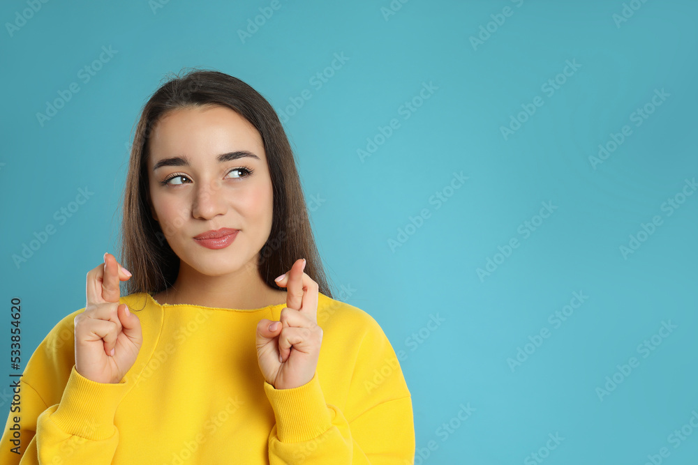 Woman with crossed fingers on light blue background, space for text. Superstition concept Woman with crossed fingers on light blue background, space for text. Superstition concept