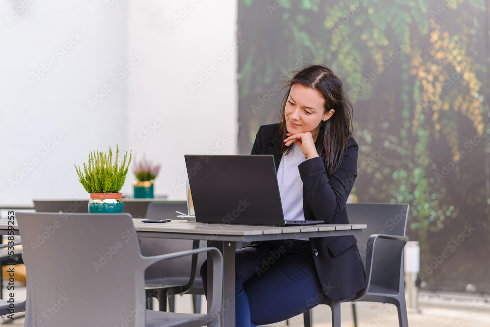 Young business woman using laptop computer.Female working on laptop in an outdoor cafe.Summer windy day. Young business woman using laptop computer.Female working on laptop in an outdoor cafe.Summer windy day.