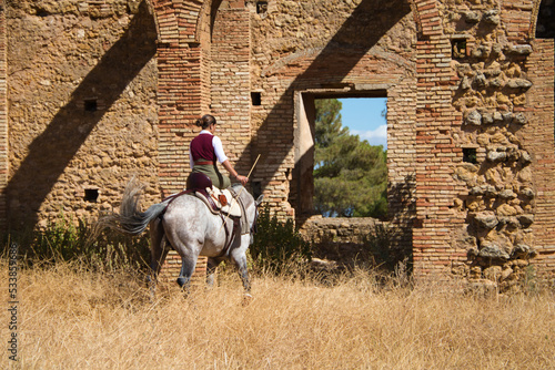 Young and beautiful Spanish woman on a Thoroughbred horse riding in the countryside in Spain. The woman is wearing a horse riding uniform. Thoroughbred and equine concept. © @skuder_photographer